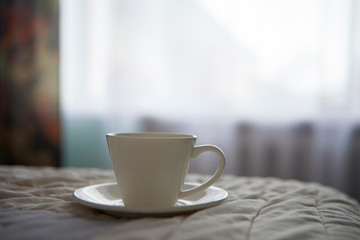 morning cup of coffee on the background of the bed and the window
