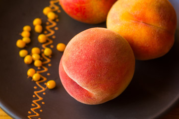 still life - juicy velvety peaches, large ripe pear, and sea buckthorn berries in a ceramic plate on a wooden background