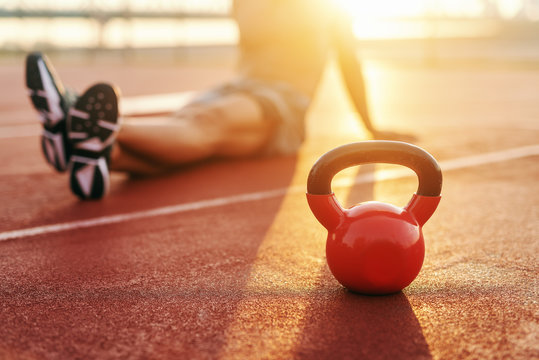 Shirtless Caucasian man sitting on court inn the morning and resting from exercising. Selective focus on kettlebell.