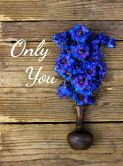 Bouquet of very bright and colorful blue delphinium flowers in a little clay vase on the rustic wooden shabby worn background, flat lay, top view, close up, copy space for you text or design