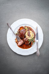 Traditionelle geschmorte Schweinebäckchen mit Kartoffelpüree und Pilzen in brauner Rotwein Sauce als Draufsicht auf einem klassisch weißen Design Teller mit Textfreiraum