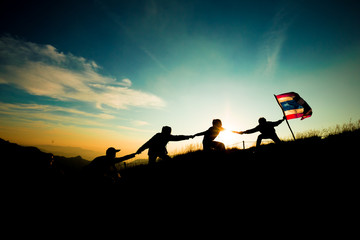 Leader handing Thailand Flag and climbers help A Team to conquer the summit in teamwork in a fantastic mountain landscape at sunset. Helping hand concept and international day of peace and teamwork.