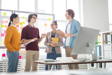 Group of four young casual colleagues brainstorming and discussing their ideas for new design...