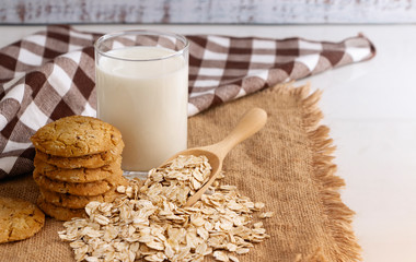 A glass of milk, cookies, and oats in spoon on the wooden table. Its are a nutrient-rich food...