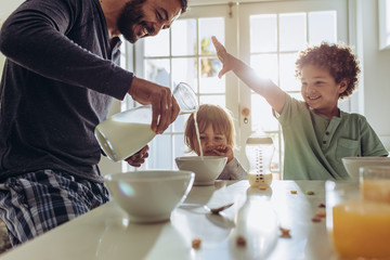 Smiling father pouring milk in to bowls for breakfast