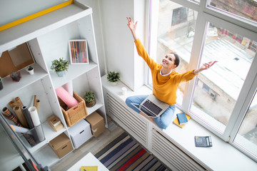 Happy young grateful businesswoman with laptop stretching her arms up while expressing triumph