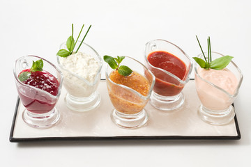Gourmet cooking concept. Set of assorted sauces. Glass gravy boats on white ceramic platter.