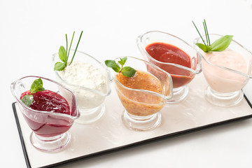 Homemade sauces composition. Assorted glass gravy boats on white platter.