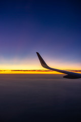 The wing of airplan in front of sunset time flying over the ocean on holiday weekend.