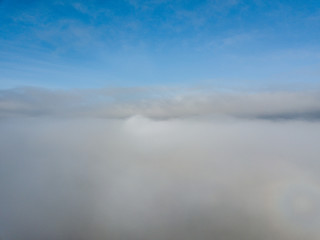 Aerial view of rural landscape in Switzerland covered with fog. Cold morning in winter with beautiful light. View from above the clouds with impressive sunlight.