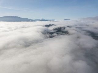 Aerial view of rural landscape in Switzerland covered with fog. Cold morning in winter with beautiful light. View from above the clouds with impressive sunlight.