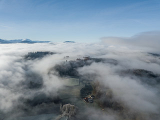 Aerial view of rural landscape in Switzerland covered with fog. Cold morning in winter with beautiful light. View from above the clouds with impressive sunlight.