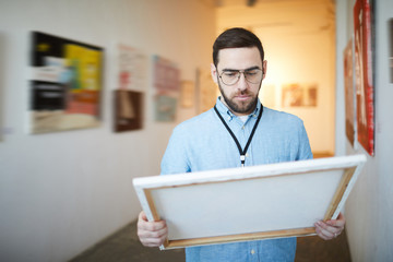 Waist up portrait of pensive bearded man holding picture in art gallery or museum, copy space