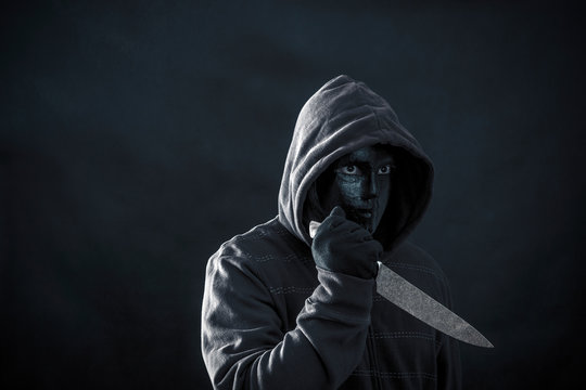 Hooded man with black mask holding knife in the dark