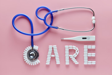 CARE word made from medicine pills and stethoscope, temperature on pink background. Concept of Valentine's Day or pharmacy, Medical.