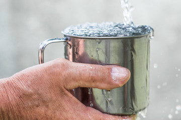 Man is holding a steel mug and a well  water is pouring from a bucket, life and thirst concept