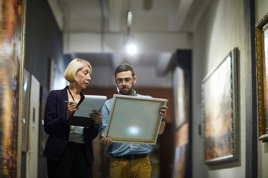 Portrait of two museum workers inspecting paintings standing in art gallery, copy space