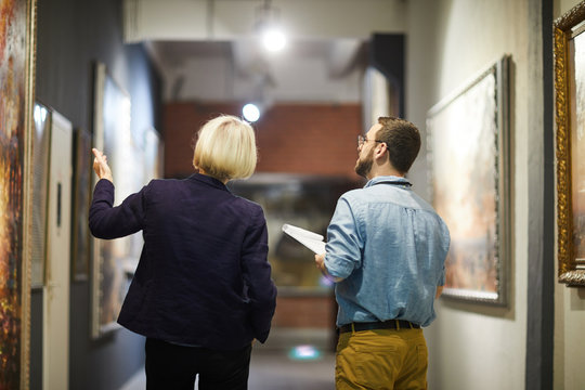 Back view portrait of two museum workers discussing paintings walking in art gallery, copy space