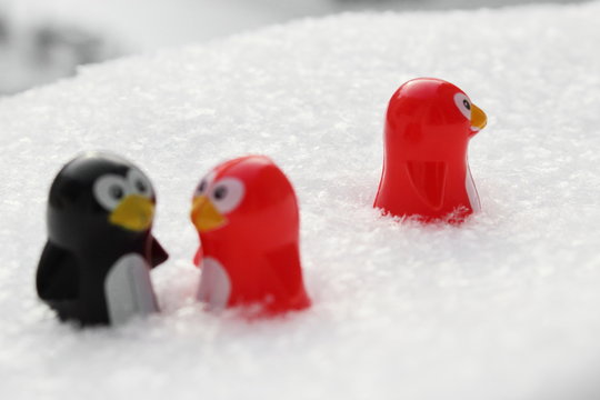 Love triangle or being third wheel. Having affair, infidelity or cheating concept. Unrequited love concept. Valentine's day concept. Three toy penguins in the snow. Focus is on the single one.