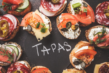 Assorted spanish tapas with fish, sausage, cheese and vegetables. Dark background, top view.