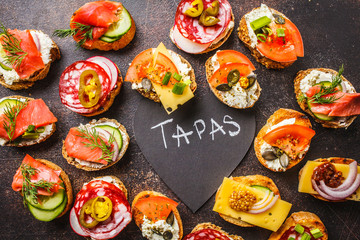 Assorted spanish tapas with fish, sausage, cheese and vegetables. Dark background, top view.