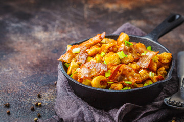 Spanish migas with pork and green onions in cast-iron pan on dark background.