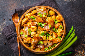 Spanish migas with pork and green onion in wooden bowl on dark background.