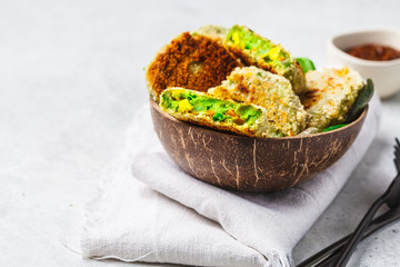 Green vegetarian burgers in coconut shell with tomato sauce on white background.