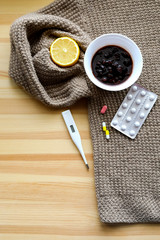 Treatment methods for throat pain, cold: thermometer, jam, lemon and tablets on the light wooden background and beige sweater