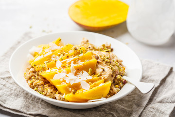 Oatmeal with mango, coconut, peanut butter and nuts in a white plate. Vegan food, healthy breakfast, plant based concept.