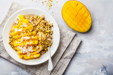 Oatmeal with mango, coconut, peanut butter and nuts in a white plate. Vegan food, healthy breakfast, plant based concept.