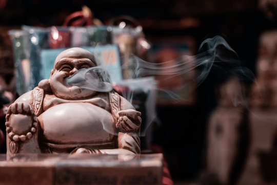 Front view of the iconic Smoking Buddha. Macro shot close up of smoke floating out of the mouth. Incense stick holder, Indian religious symbol, yoga and meditation concept.