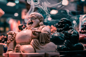 Obraz premium Side view of the iconic Smoking Buddha. Macro shot close up of smoke floating out of the mouth. Incense stick holder, Indian religious symbol, yoga and meditation concept.