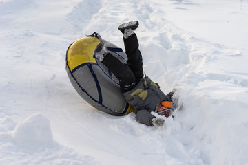 A child rolls from a snowy mountain and falls from a tubing.