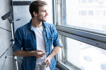 Smiling young man talking on mobile phone, looking at the window at home.