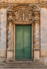 Fototapeta na wymiar Green front door with stone carving in Ortigia island near Syracuse, Sicily, Italy 