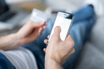 Online payment. Man's hands holding a credit card and using smart phone for online shopping.
