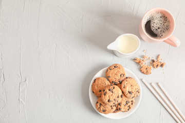 Plate with tasty chocolate chip cookies and cup of coffee on gray background, top view. Space for text