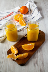 Fresh orange juice in glass jars over white wooden background, low angle view. Closeup.