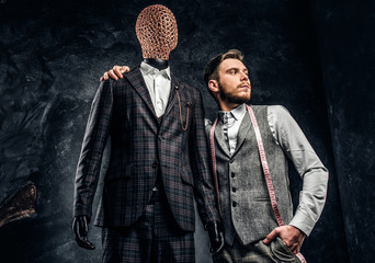 A confident fashion designer posing next to a mannequin in exclusive custom made men's suit in a...