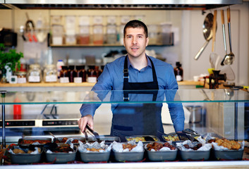 Young business owner standing behind the counter of his restaurant. Kitchen behind