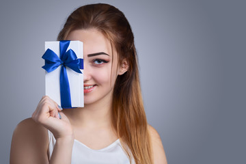 portrait of a happy woman with a gift box in her hands on a studio background, the girl covers half...