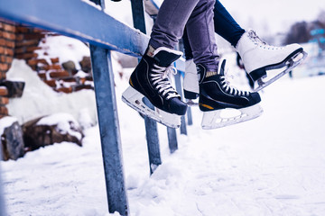 Couple wearing ice skates sitting on a guardrail. Dating in an ice rink.