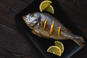 Baked sea bream with lemon, on dark background.