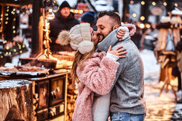A cheerful attractive couple in love, enjoying spending time together while embracing at the winter fair at a Christmas time