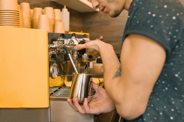 Young male coffee shop worker making coffee with machine