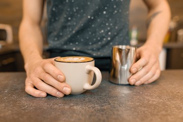 Close up of baristas hands and freshly prepared art coffee with foam and pattern