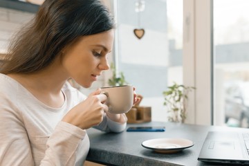 Closeup of young beautiful woman in profile with cup of fresh coffee in coffee shop