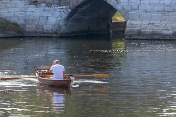 man in rowing boat scratches head with ancient stone bridge arch in the background