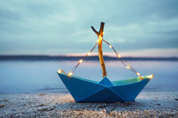 magisches Papierboot mit Lichterkette am Strand